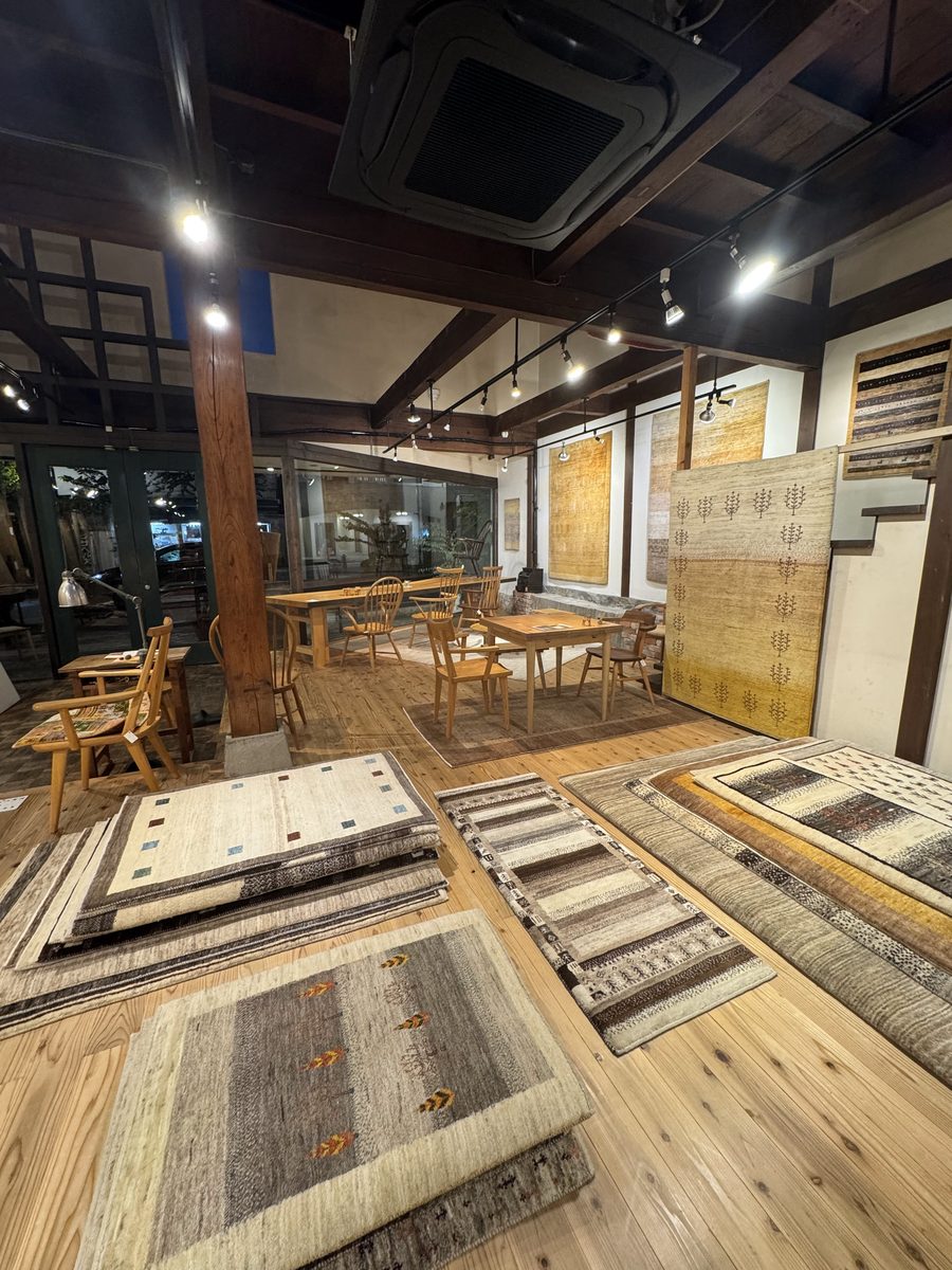 松葉屋家具店の店内。一枚板のテーブルと椅子のあいだに、ギャッベを広げたところ